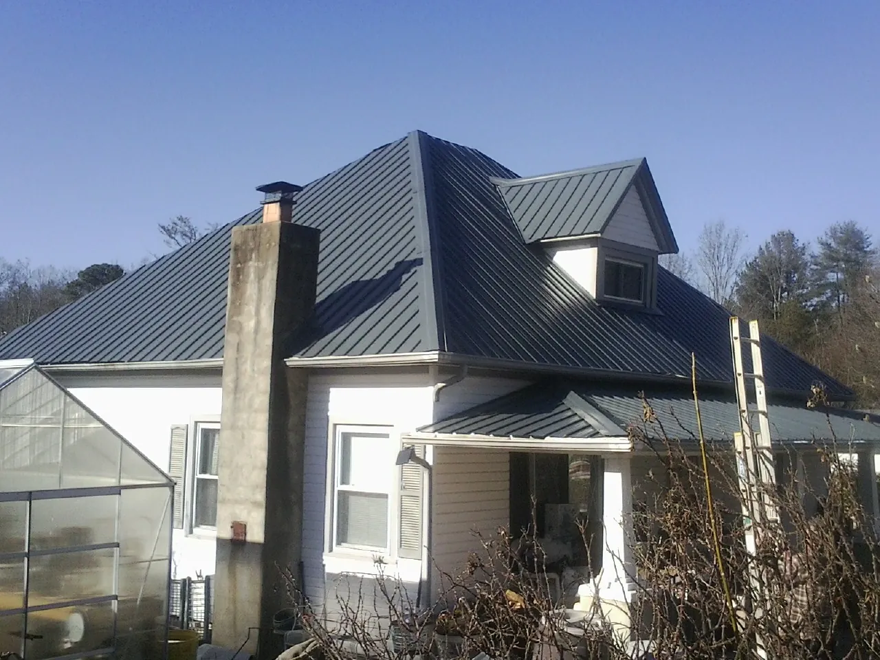 Dark blue standing seam metal roof on a white farmhouse with dormer — Slate & Tile Roof Repair by Roofing Brothers in Birchwood