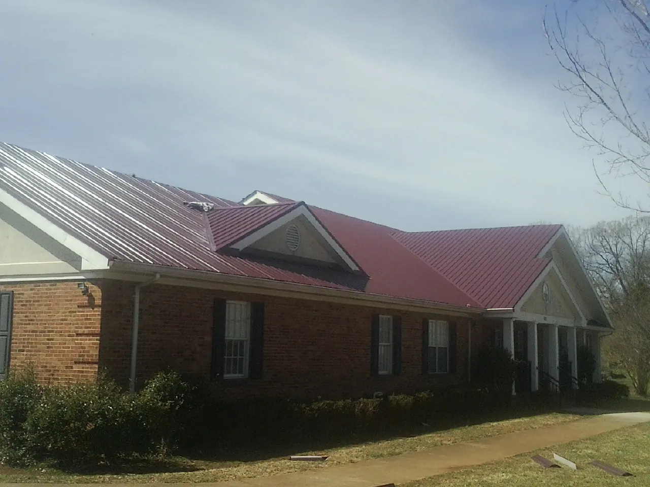 Red metal roof with gabled entries on a long brick building, from a Hail Damage Roof Repair job in Birchwood