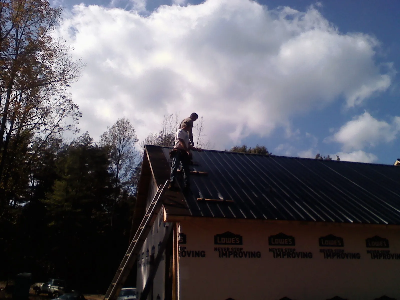 Roofer fastening dark metal panels high against a cloudy sky, from a Roof Inspection job in Birchwood