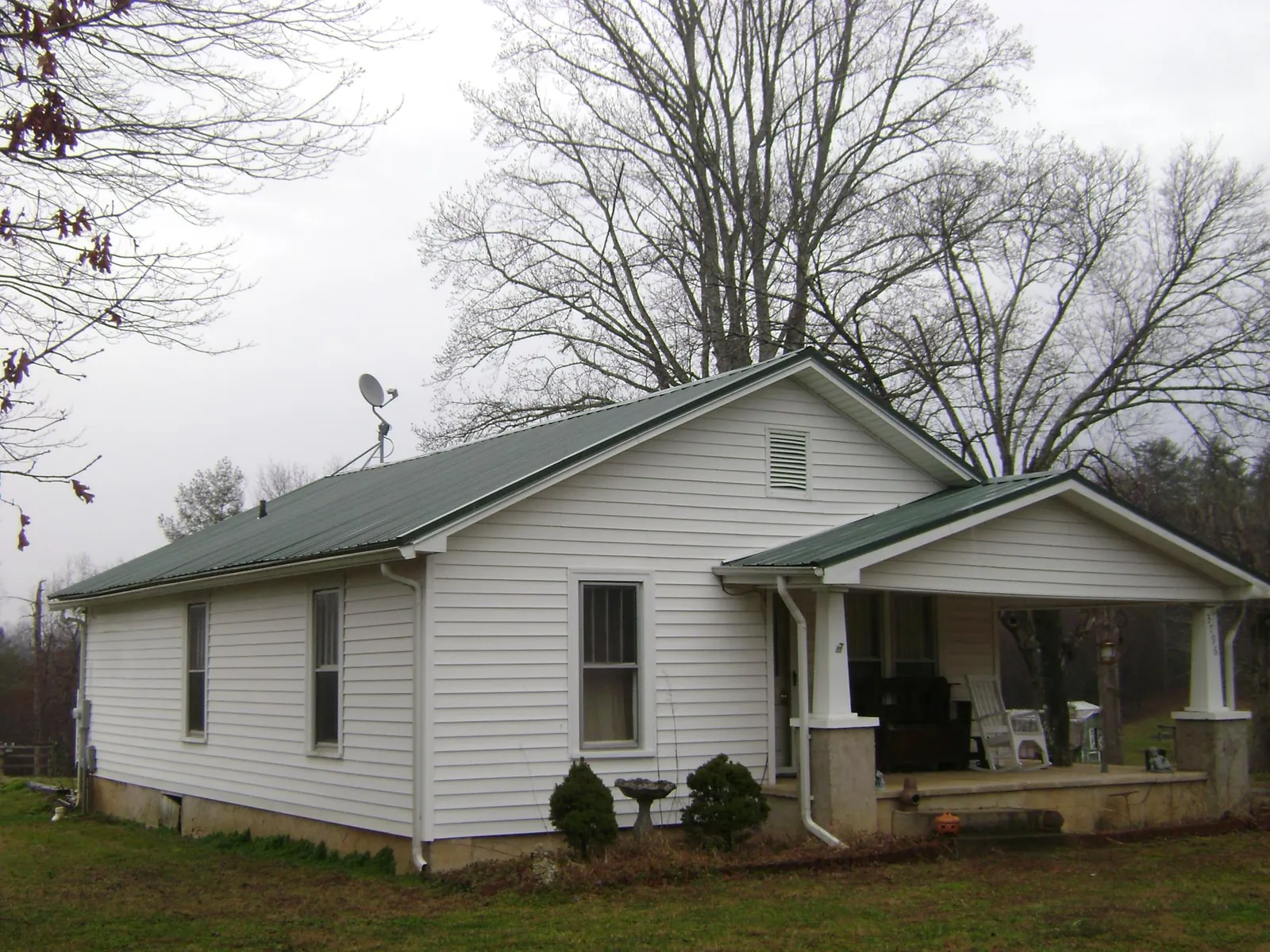 Green metal roof on a white bungalow with a side porch in Birchwood