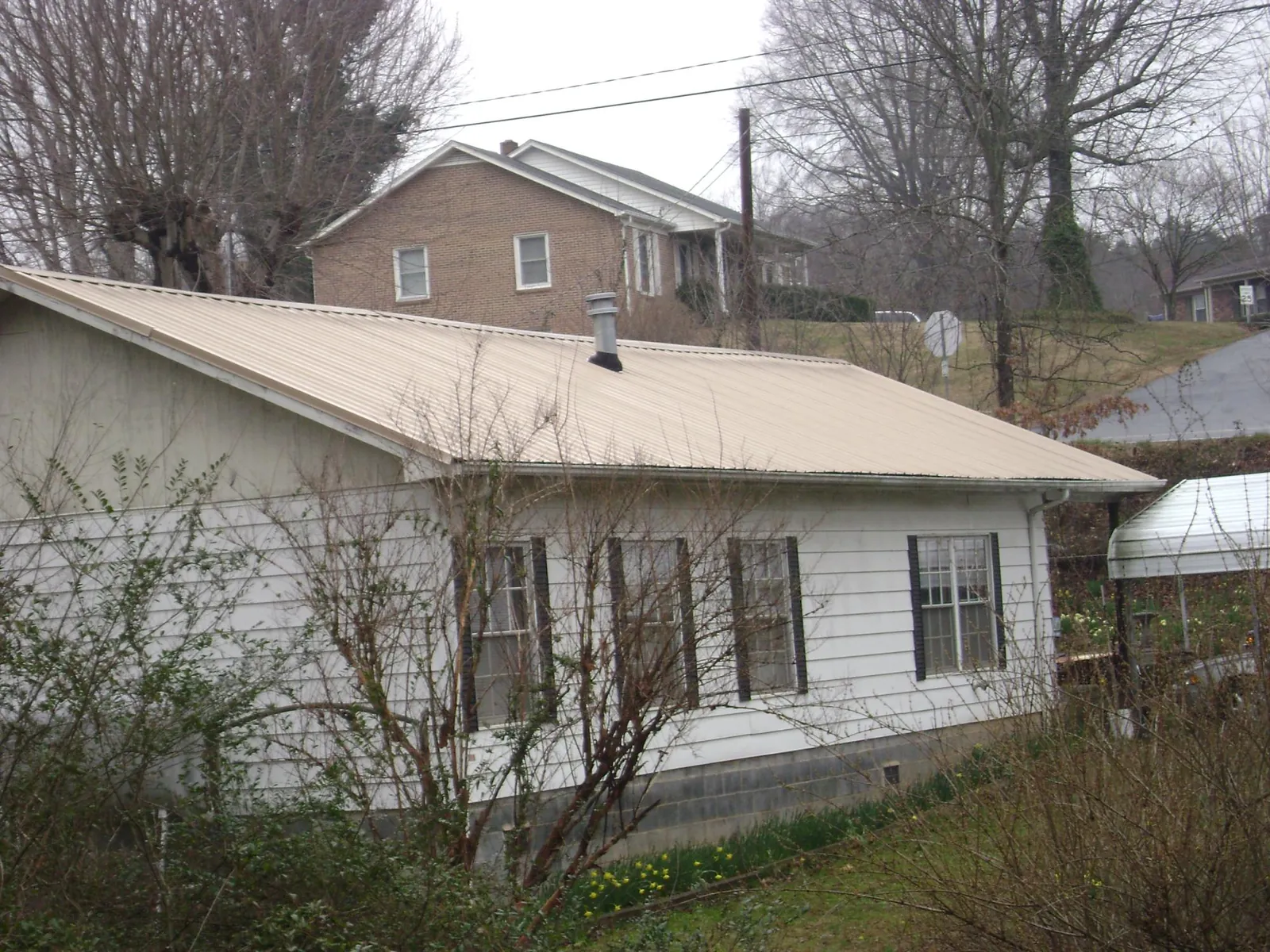 Tan metal roof on a white sided house set into a hillside — Commercial Roofing by Roofing Brothers in Birchwood