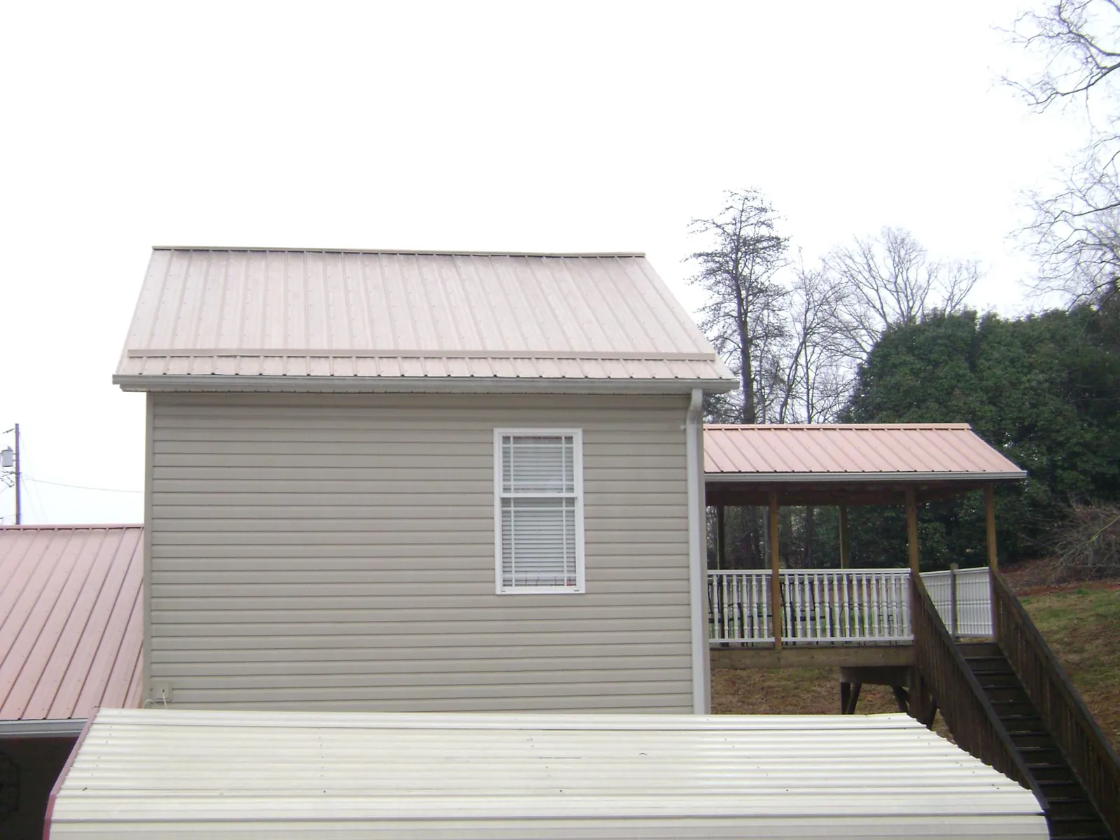 Tan metal roofs on a two story addition and attached porch, from a Roof Replacement job in Birchwood